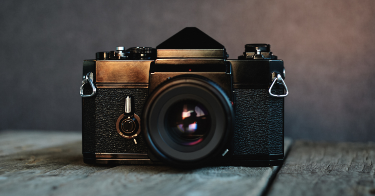 Vintage-Kamera auf einem Holztisch, mit unscharfem Hintergrund – Produktfoto mit Fokus auf das Kameraobjektiv.
